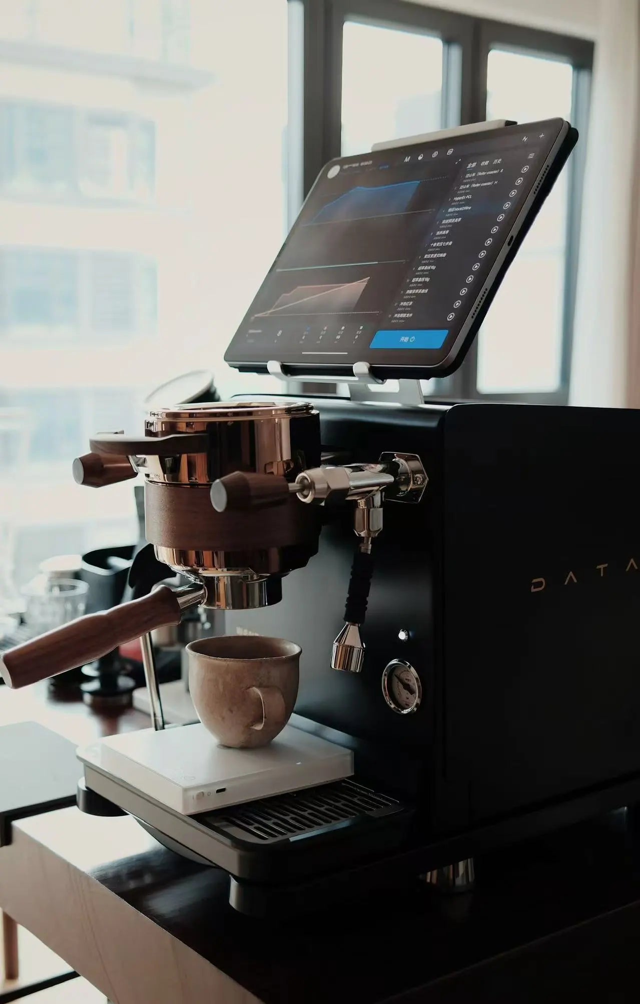 the Wendougee DATA S an high end Espresso machine with a tablet that show the profile that was extracted on top of the machine, sitting on a Coffee table ready to for the next brew, with the cup on an espresso scale. vellutto.eu